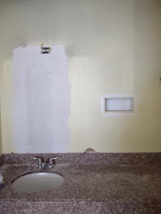 The wall behind the bathroom mirror has been repaired and prepped for painting. Then a new mirror will be installed.
