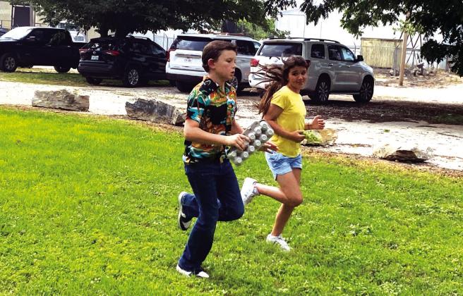 The students are participating in the Recycle Race. The recycle race is a race where the student picks up an item at the starting line, races down to the other end where containers for trash, recycle, compost, and repurpose/donate are staged and the student determines while racing down where the item goes, putting it in the corresponding container. There are also volunteers by the containers to agree with the student or correct. The student then races back to tag the next person in line.