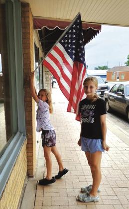 Abby (left) and Hadley (right) Fuller were hanging this American flag at the news office prior to Memorial Day. Photo by Djuana Payton