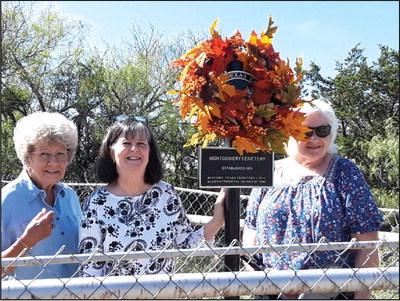 Barbara Maddox (Secretary/Treasurer), Betty Fowler (Historian), and Jan Root (President) posing with the wreathed drapped Historical Marker