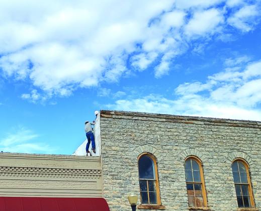Jake Uptain is climbing up the next level of roof while he grabs the hand of G. T. Meador and Kyle Anderson gives him a boost.