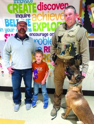 Jake Lackey, Ian Merriman and Andor present pencils and bookmarks to San Saba Elementary student Hudson Turner.
