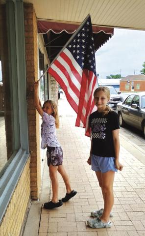 Abby (left) and Hadley (right) Fuller were hanging this American flag at the news office prior to Memorial Day. Photo by Djuana Payton