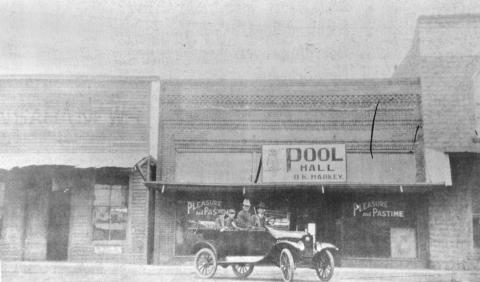 PLEASURE AND PASTIME––so says the sign on the O. K. Harkey Pool Hall and notice how convenient it was to the San Saba News Office (at left). Our thanks to Margaret C. Joiner of Austin who provided the picture. The only notation is the “Bud” Joiner is the driver of the car. The picture was found among the belongings of Mrs. L. L. (Josie) Joiner. Anybody remember the year?